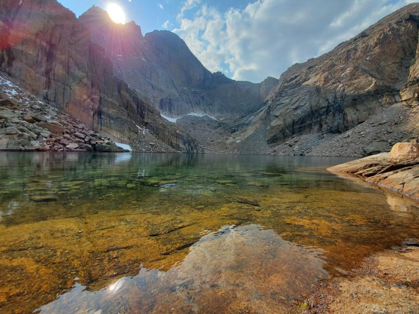 Sun cresting the ridge above an alpine lake